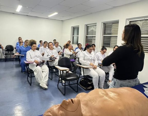 O Hospital Municipal Dr. Waldemar Tebaldi, em Americana, realizou neste mês um treinamento teórico e prático de reanimação cardiopulmonar (RCP) voltado às equipes assistenciais da unidade. A capacitação teve como objetivo atualizar conhecimentos, padronizar condutas e aprimorar a resposta dos profissionais diante de situações de parada cardiorrespiratória. Conduzido pela Dra. Eloisa Duzzi, médica que atua na Emergência do HM, o treinamento abordou os principais protocolos de atendimento, reunindo conteúdos teóricos e atividades práticas com manequins para simulação. A proposta foi fortalecer a atuação integrada das equipes e ampliar a segurança no atendimento aos pacientes em situações críticas. Segundo Dra. Eloisa, a atualização constante dos profissionais é essencial para garantir uma assistência segura e eficaz. "Na parada cardiorrespiratória, cada segundo faz diferença. Por isso, é fundamental que toda a equipe esteja preparada para reconhecer rapidamente a situação, iniciar as manobras corretas e atuar de forma coordenada. O treinamento prático permite aperfeiçoar habilidades técnicas e aumentar a confiança dos profissionais para agir em momentos decisivos", destacou. A iniciativa integra o programa permanente de educação continuada desenvolvido pelo Hospital Municipal, que promove regularmente treinamentos voltados ao aprimoramento técnico das equipes e ao fortalecimento da cultura de segurança do paciente. "A qualificação permanente dos profissionais é uma das prioridades da Secretaria de Saúde, porque sabemos que equipes bem treinadas fazem toda a diferença na assistência prestada à população. A reanimação cardiopulmonar é um procedimento que exige rapidez, precisão e integração entre os profissionais, e esse tipo de capacitação reforça a preparação das equipes para agir com segurança em situações de emergência. Seguiremos investindo em educação continuada para fortalecer cada vez mais a qualidade do atendimento oferecido no Hospital Municipal", comentou o secretário adjunto de Saúde, Fábio Joner. "Investir na formação contínua das equipes é investir diretamente na segurança do paciente. Treinamentos como este garantem que os profissionais estejam atualizados, preparados para atuar com agilidade e alinhados às melhores práticas assistenciais, contribuindo para um atendimento cada vez mais seguro e de qualidade", afirmou a gerente assistencial do HM, Sarah Guimarães. O Hospital Municipal Dr. Waldemar Tebaldi é administrado pelo Grupo Chavantes, em gestão compartilhada com a Secretaria Municipal de Saúde da Prefeitura de Americana.