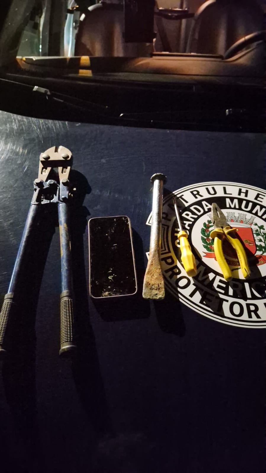 A Guarda Municipal de Americana (GAMA) deteve, na noite desta quarta-feira (16), um homem suspeito de tentativa de furto de fios na Unidade Básica de Saúde (UBS) do Jardim Boer. A ocorrência foi registrada por volta das 21h19, quando uma equipe da GAMA, durante patrulhamento, encontrou um veículo Fiat Uno branco estacionado ao lado do alambrado da unidade. O automóvel estava aberto e não havia ninguém nas proximidades. Durante a averiguação, os agentes constataram que parte do alambrado havia sido levantada. No interior da UBS, foram identificadas duas caixas de energia com as tampas abertas e fios puxados. Diante da situação, equipes de apoio foram acionadas para realizar uma busca no local. Durante a averiguação das proximidades, os agentes visualizaram um homem saindo de trás de um muro, em uma área de vegetação próxima à unidade. Ele foi abordado e informou ser o proprietário do veículo. Nas buscas realizadas na área de mata, os agentes localizaram um alicate corta-vergalhão de grande porte. Dentro do terreno da UBS, próximo à caixa principal de energia e ao muro que dá acesso à área de vegetação, também foi encontrada uma talhadeira. Os fios da caixa apresentavam sinais de terem sido puxados. Questionado sobre os fatos, o homem negou a tentativa de furto. Diante dos indícios constatados no local, ele e as ferramentas encontradas foram encaminhados ao Plantão Policial para apresentação da ocorrência à autoridade policial. A perícia compareceu à UBS para realizar os procedimentos necessários. O homem permaneceu à disposição da Justiça. O veículo foi recolhido ao pátio por estar estacionado irregularmente em praça ou jardim público, conforme o artigo 181, inciso VII, do Código de Trânsito Brasileiro.